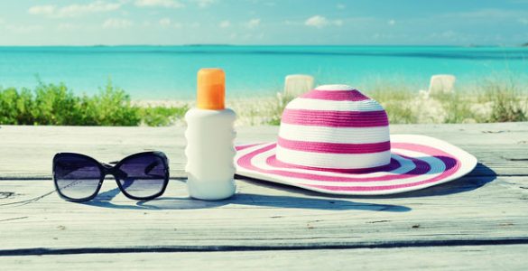 Sun hat, sun glasses and sun lotion on a table overlooking a beach