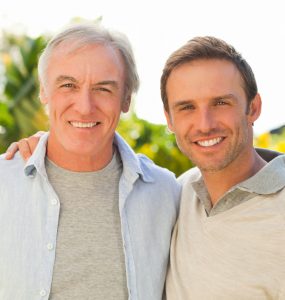 A middle-aged man and grown up son smiling
