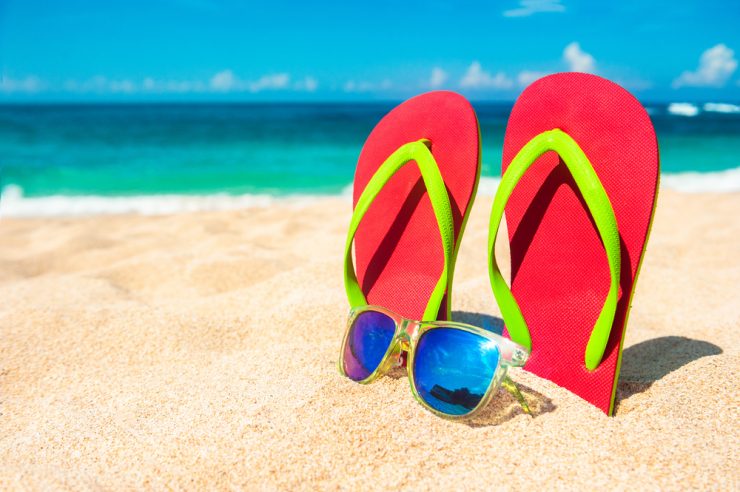 Flip floops and sunglasses on a beach with the sea in the background representing summer holidays