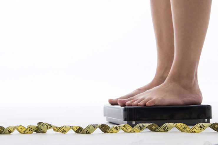Close up on woman's feet on a pair of scales next to a measuring tape