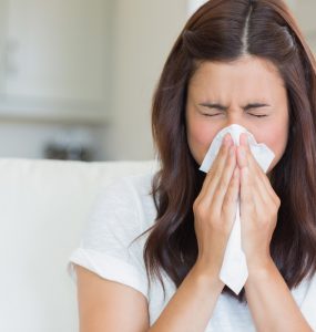 Close up of woman with a cold blowing her nose with a tissue.