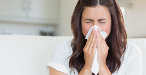 Close up of woman with a cold blowing her nose with a tissue.