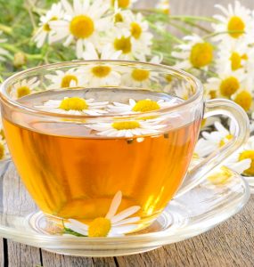 CLose up of a cup of camomile tea surrounded by camomile flowers