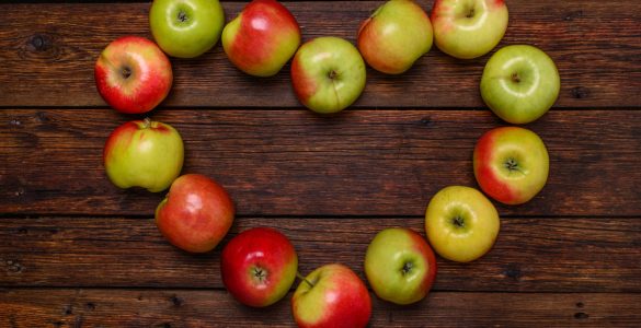 Red and green apples arranged in a heart shape on a wooden background