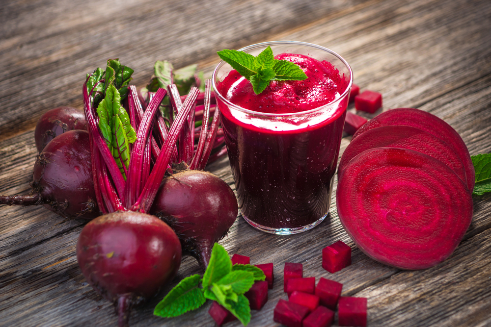 Whole and sliced beetroot surrounding a glass of beetroot juice