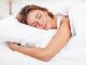 Woman hugging pillow whilst sleeping in bed