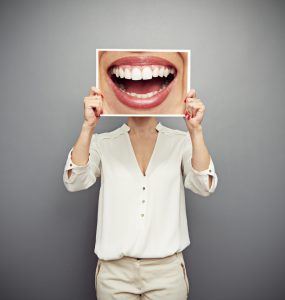 Woman holding an oversized photo of a smiling mouth over her face