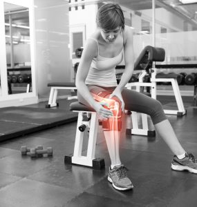Woman at the gym sitting on a bench with joint pain indicated by a red glow around her knee