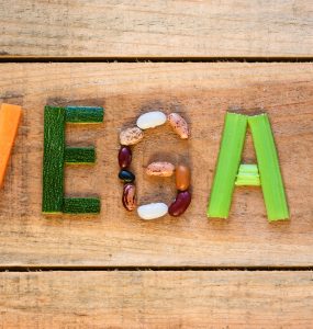 Vegetables laid out on wooden background to spell the word vegan