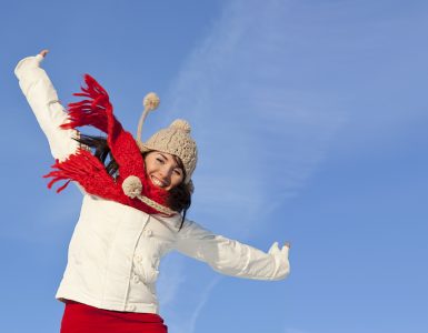 Woman in hat and scarf jumping wiht energy outdoors