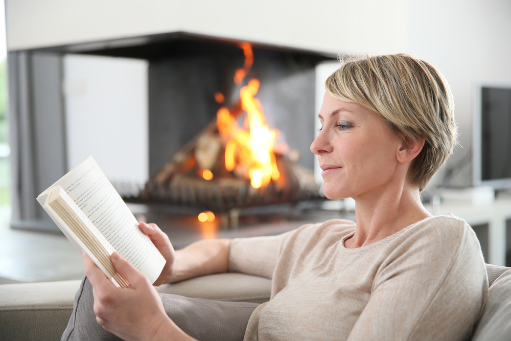 Close up of middle aged woman reading a book in front of a fire place