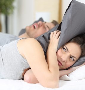 Wmoan with pillow over her head in bed whilst partner snores