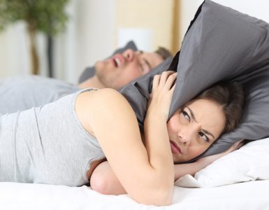 Wmoan with pillow over her head in bed whilst partner snores